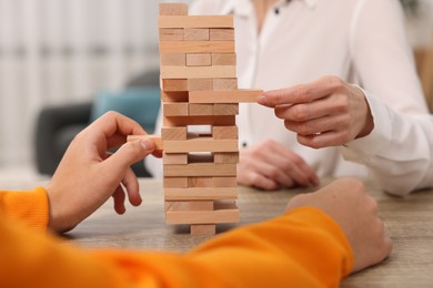 People playing Jenga tower at wooden table indoors, closeup