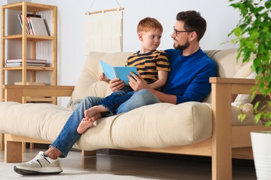 Photo of Father reading book with his son on sofa in living room at home