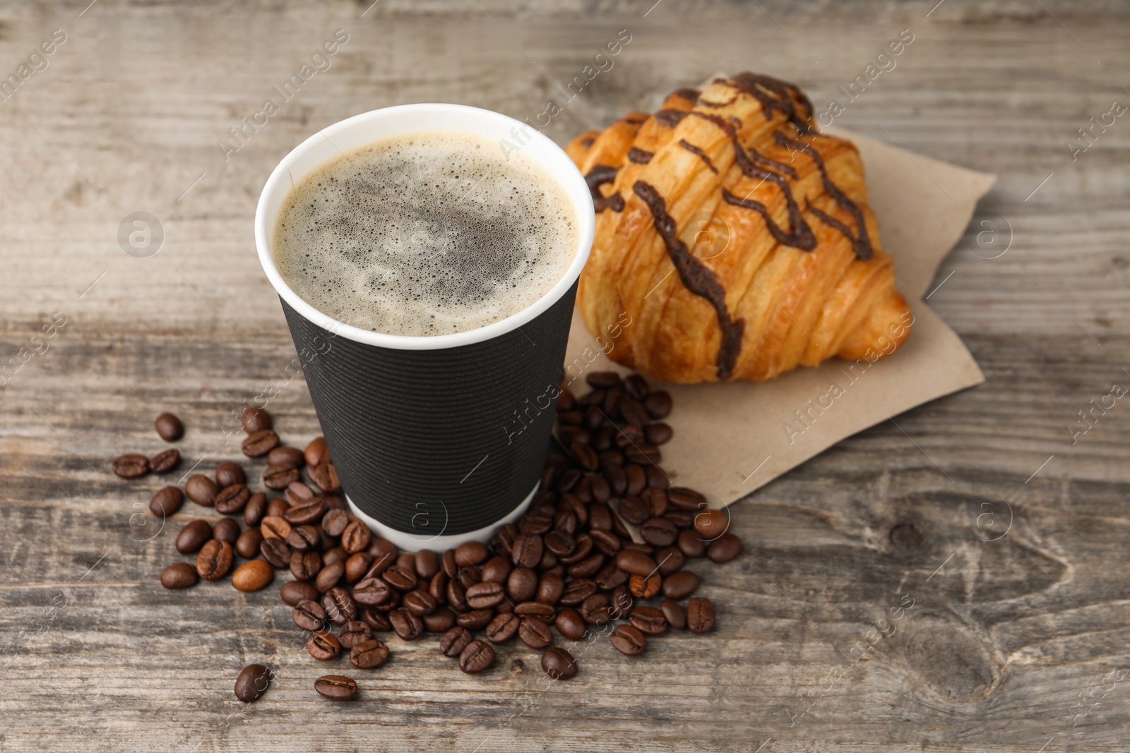 Photo of Coffee to go. Paper cup with tasty drink, beans and croissant on wooden table