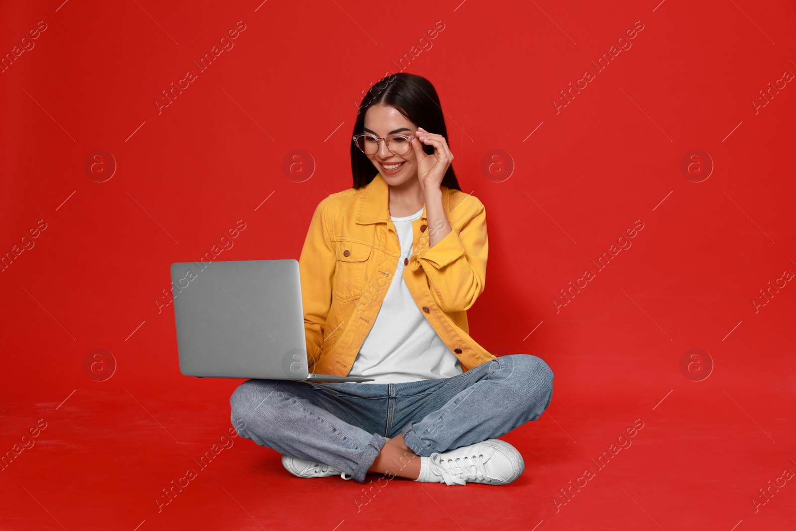 Photo of Young woman with modern laptop on red background