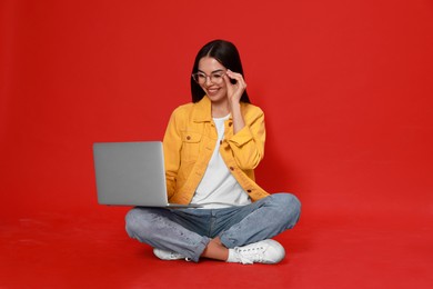 Young woman with modern laptop on red background