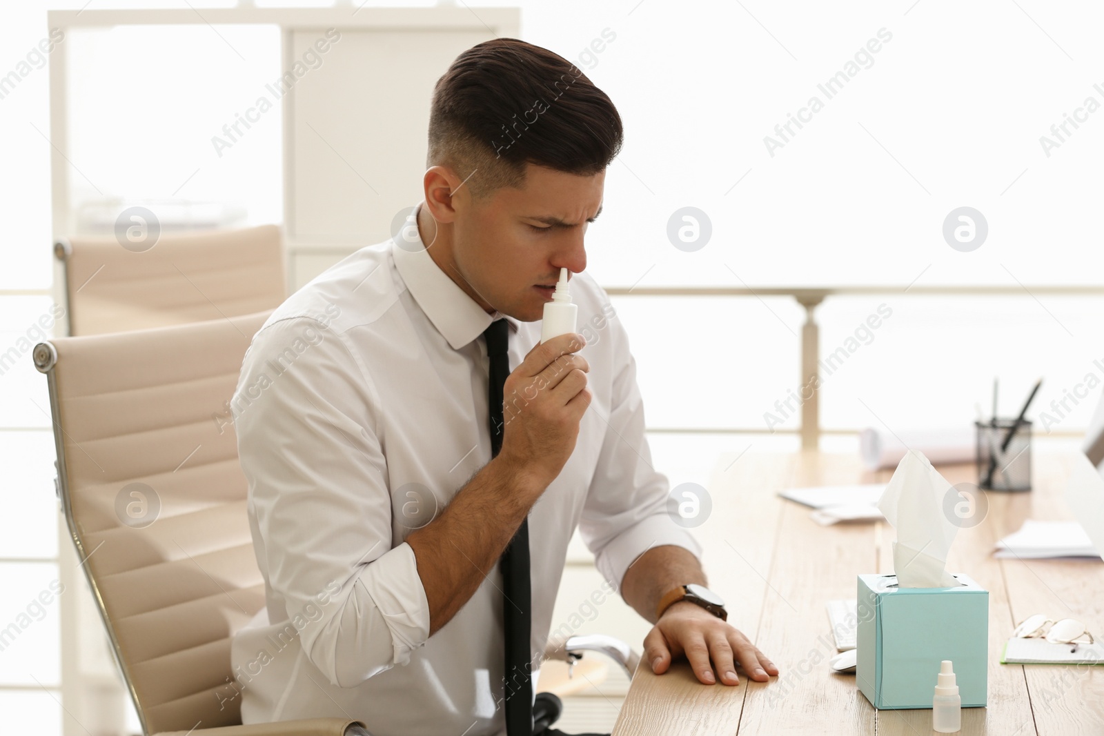 Photo of Ill businessman using nasal spray at table in office