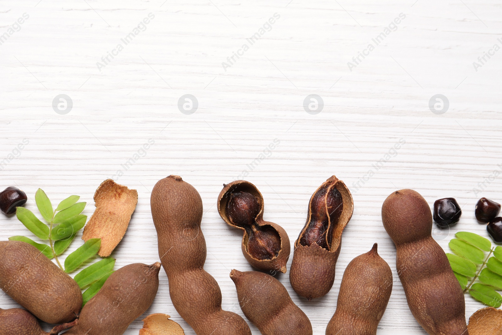 Photo of Delicious ripe tamarinds and leaves on white wooden table, flat lay. Space for text