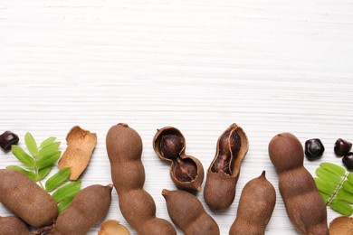 Delicious ripe tamarinds and leaves on white wooden table, flat lay. Space for text