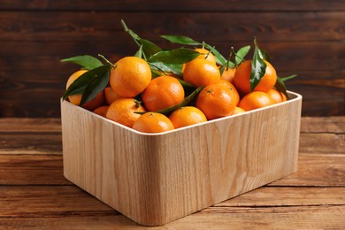 Photo of Fresh tangerines with green leaves in crate on wooden table