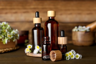 Photo of Bottles of chamomile essential oil and flowers on wooden table