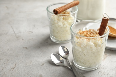 Photo of Creamy rice pudding with cinnamon in glasses served on grey table. Space for text