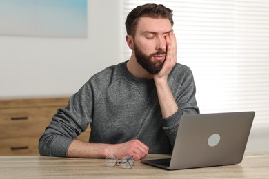 Overwhelmed man sitting with laptop at table indoors