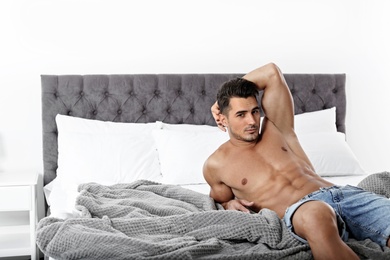 Photo of Sexy young man lying on bed with soft pillows at home