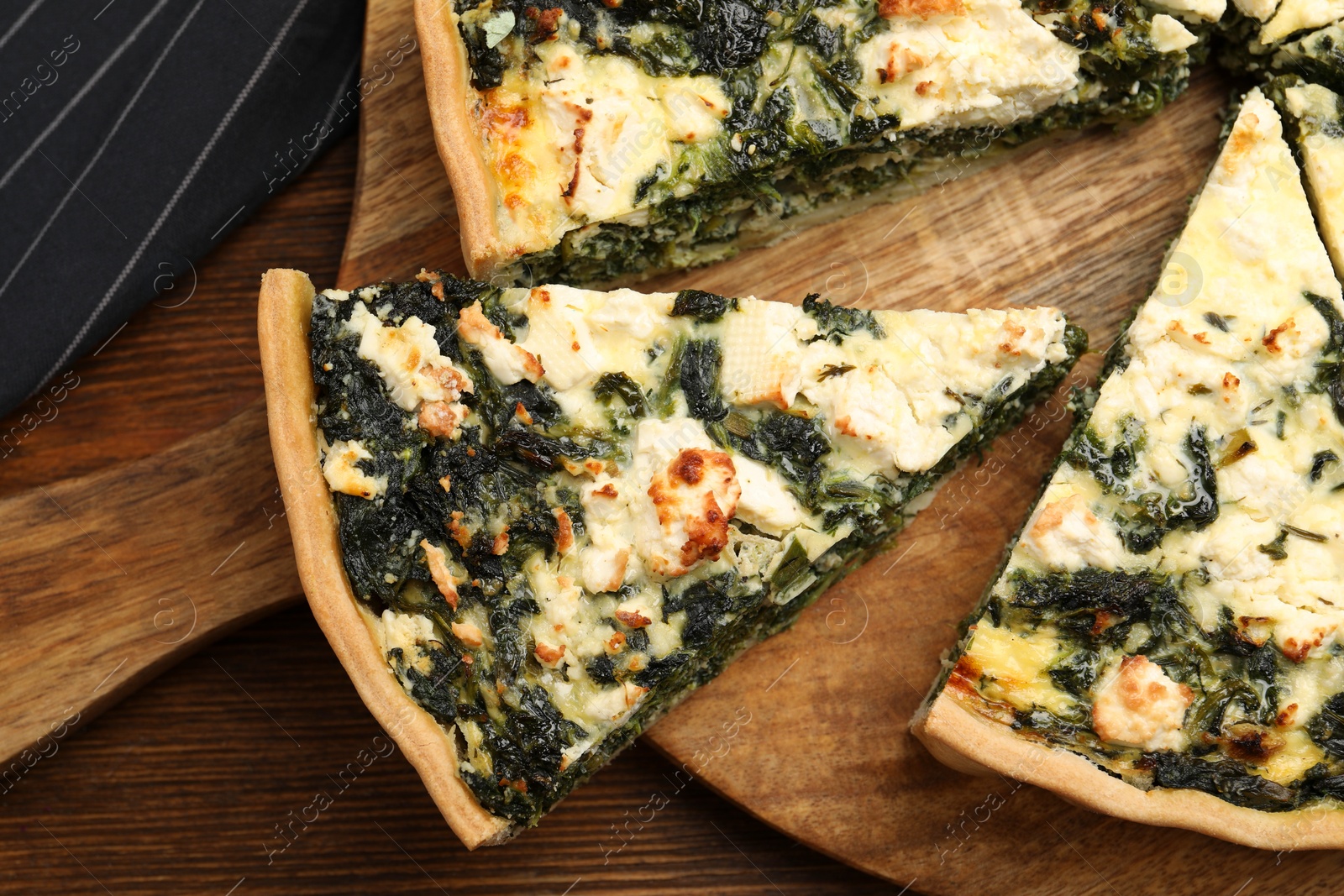 Photo of Delicious homemade spinach quiche on wooden board, closeup