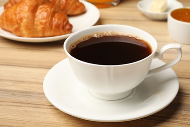 Photo of Cup of tasty aromatic coffee and croissants for breakfast on wooden table