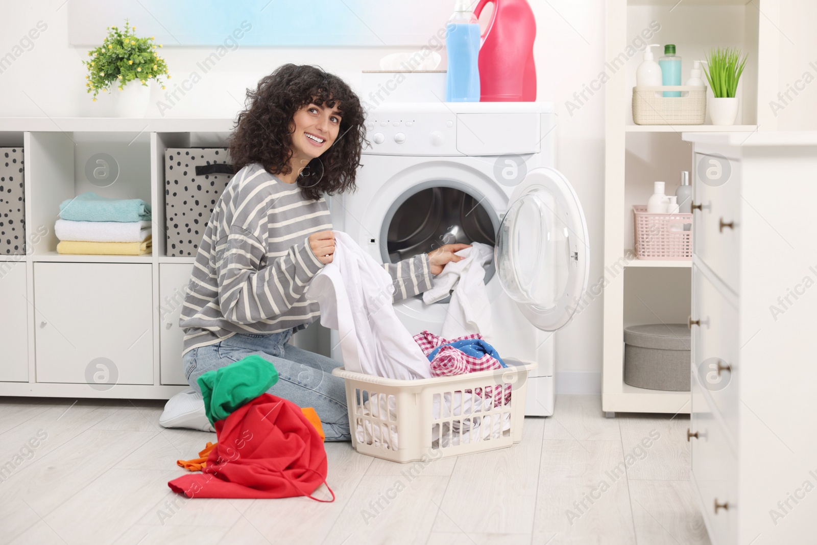 Photo of Happy woman putting laundry into washing machine indoors