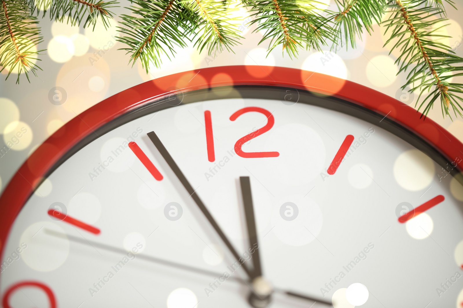 Image of Clock showing five minutes till midnight with fir tree branches, closeup with bokeh effect. New Year countdown