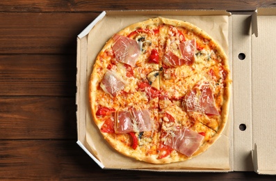 Carton box with delicious pizza on wooden background, top view