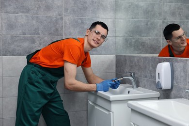 Photo of Smiling plumber repairing faucet with spanner in bathroom