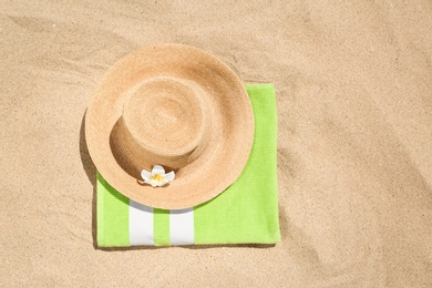 Photo of Straw hat with green towel and space for text on golden sand, flat lay. Beach objects