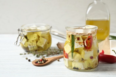 Photo of Jar with feta cheese marinated in oil on white wooden table. Pickled food