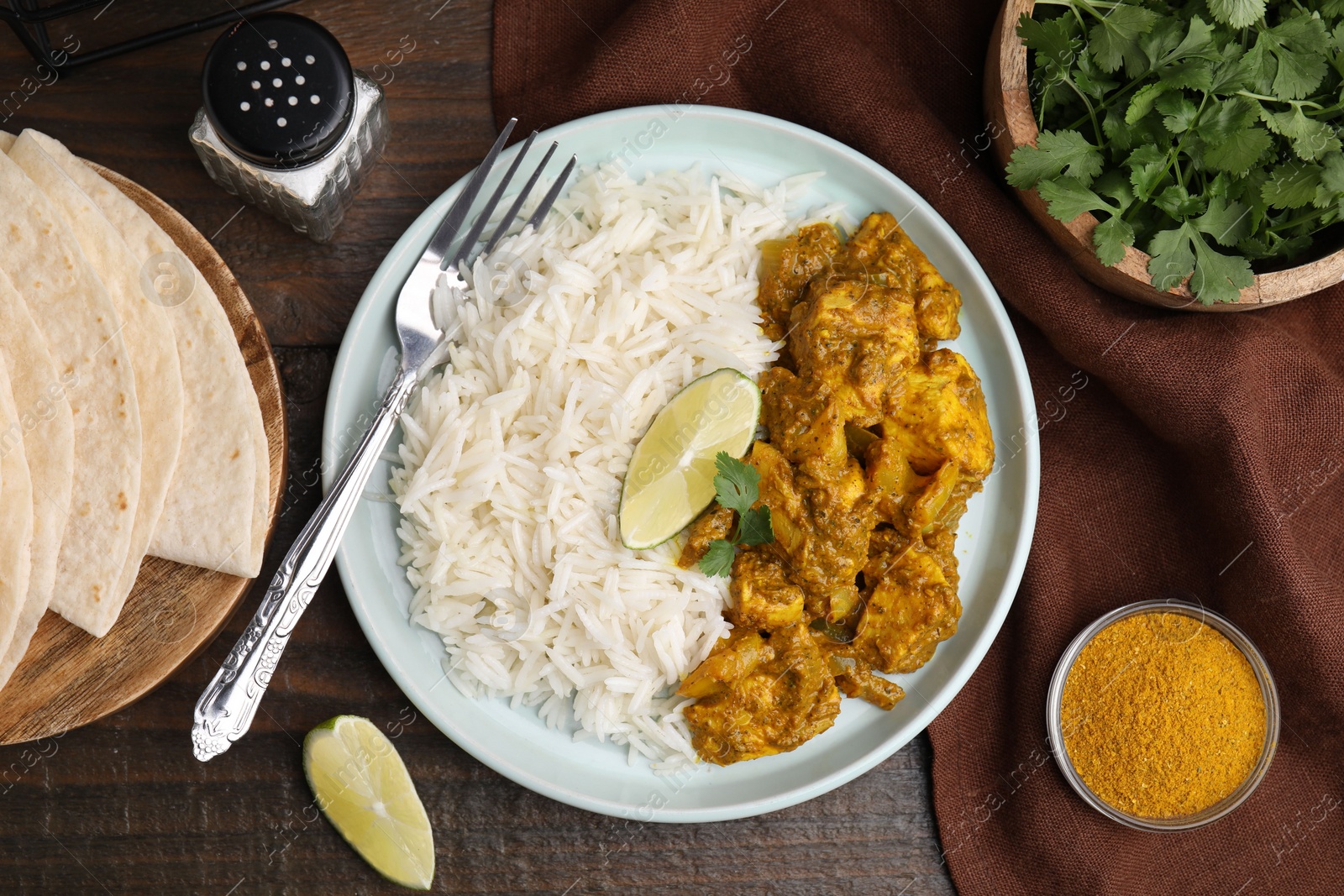 Photo of Delicious chicken curry with rice and ingredients on wooden table, flat lay