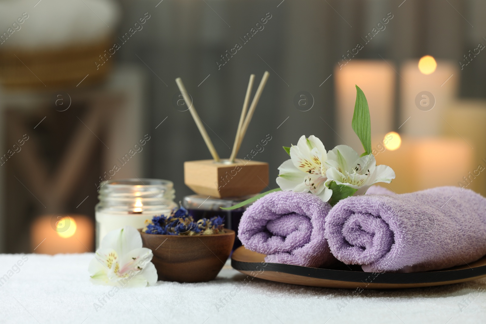 Photo of Beautiful composition with different spa products and flowers on white towel against blurred background