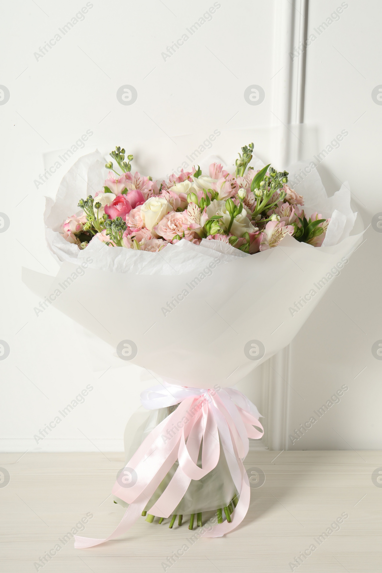 Photo of Beautiful bouquet of fresh flowers on wooden table near white wall