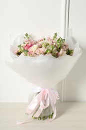 Beautiful bouquet of fresh flowers on wooden table near white wall