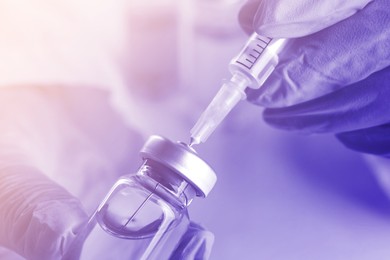 Doctor filling syringe with medication from vial, closeup. Color toned