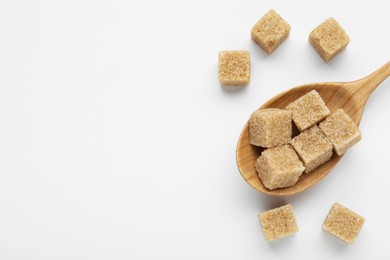 Brown sugar cubes in wooden spoon on white background, top view. Space for text