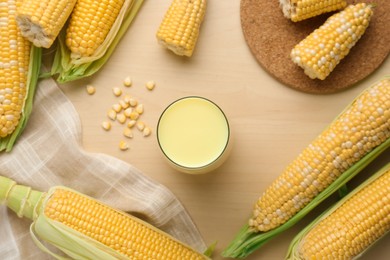 Photo of Corn juice and cobs on wooden table, flat lay
