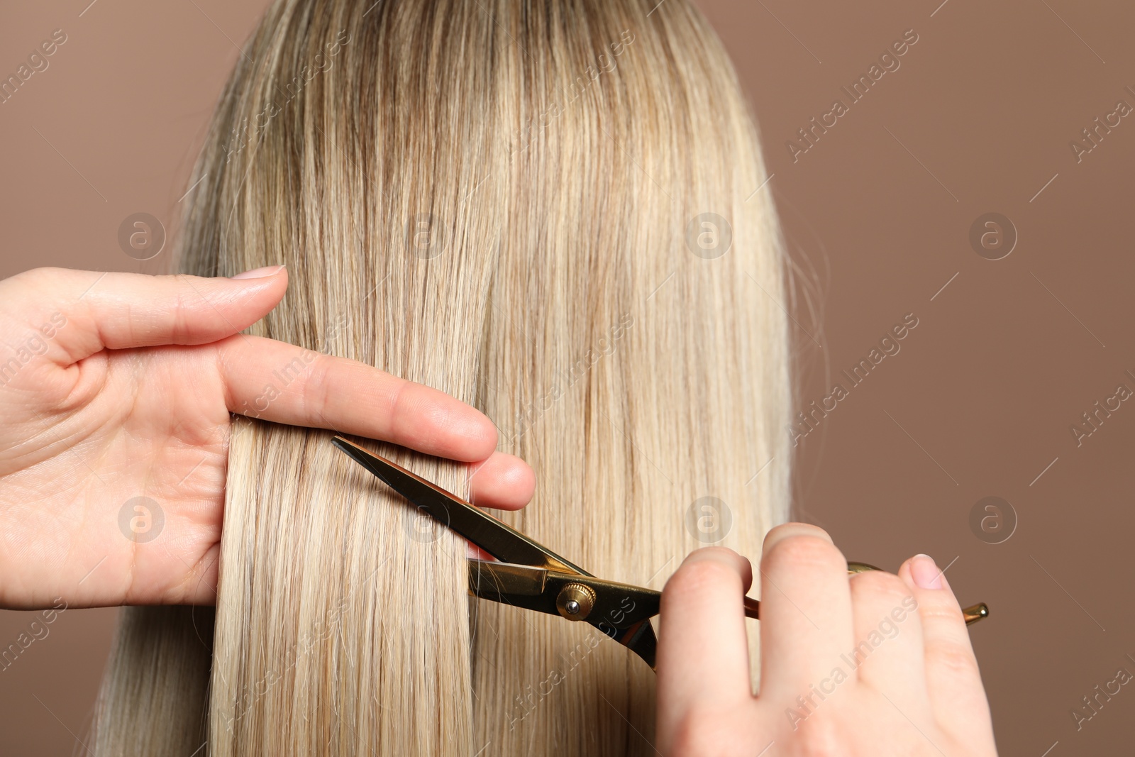 Photo of Hairdresser cutting client's hair with scissors on light brown background, closeup