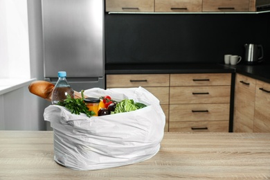 Photo of Plastic bag with vegetables and other products on wooden table in kitchen. Space for text
