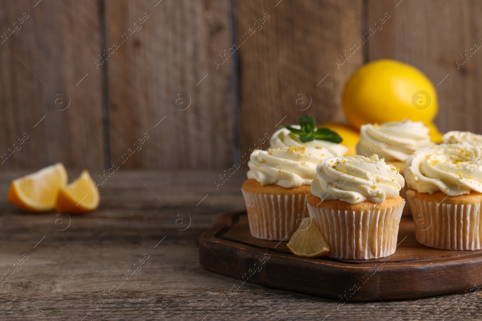 Photo of Delicious cupcakes with white cream and lemon zest on wooden table, closeup. Space for text