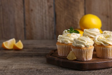 Delicious cupcakes with white cream and lemon zest on wooden table, closeup. Space for text