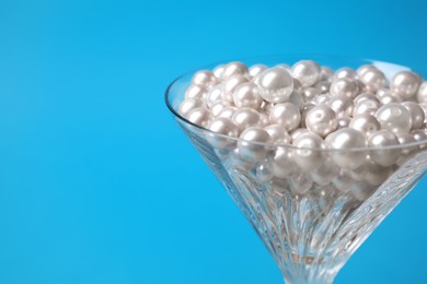 Beautiful martini glass with pearls on light blue background, closeup. Space for text