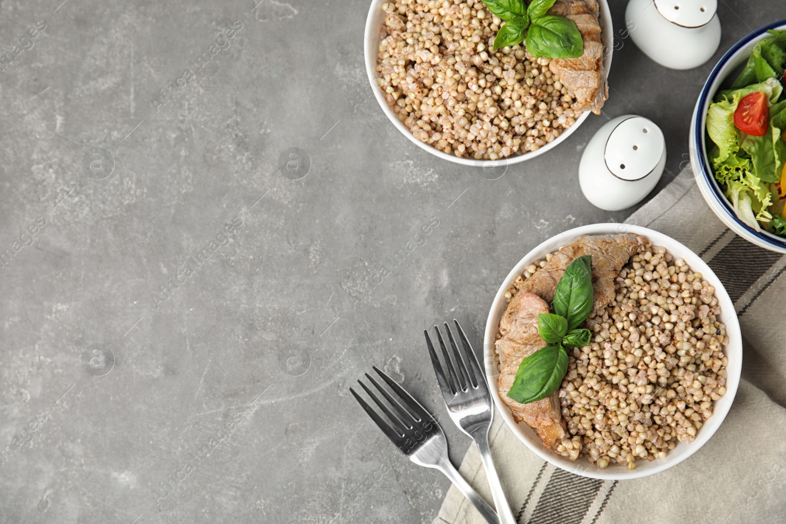 Photo of Tasty buckwheat porridge with meat on grey table, flat lay. Space for text