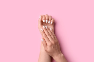 Woman showing her manicured hands with white nail polish on pink background, top view
