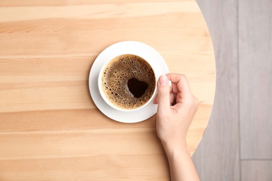 Photo of Young woman with cup of delicious hot coffee at table, top view