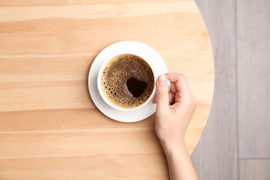 Young woman with cup of delicious hot coffee at table, top view