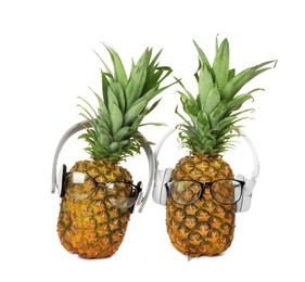 Photo of Fresh pineapples with headphones and glasses on white background