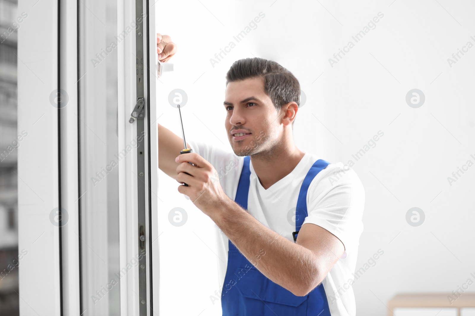 Photo of Construction worker repairing plastic window with screwdriver indoors