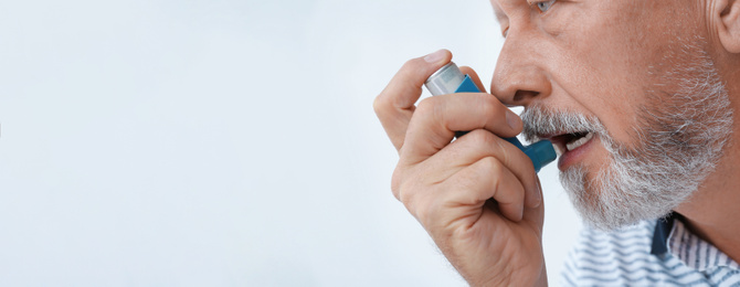 Image of Closeup view of man using asthma inhaler on white background, space for text. Banner design