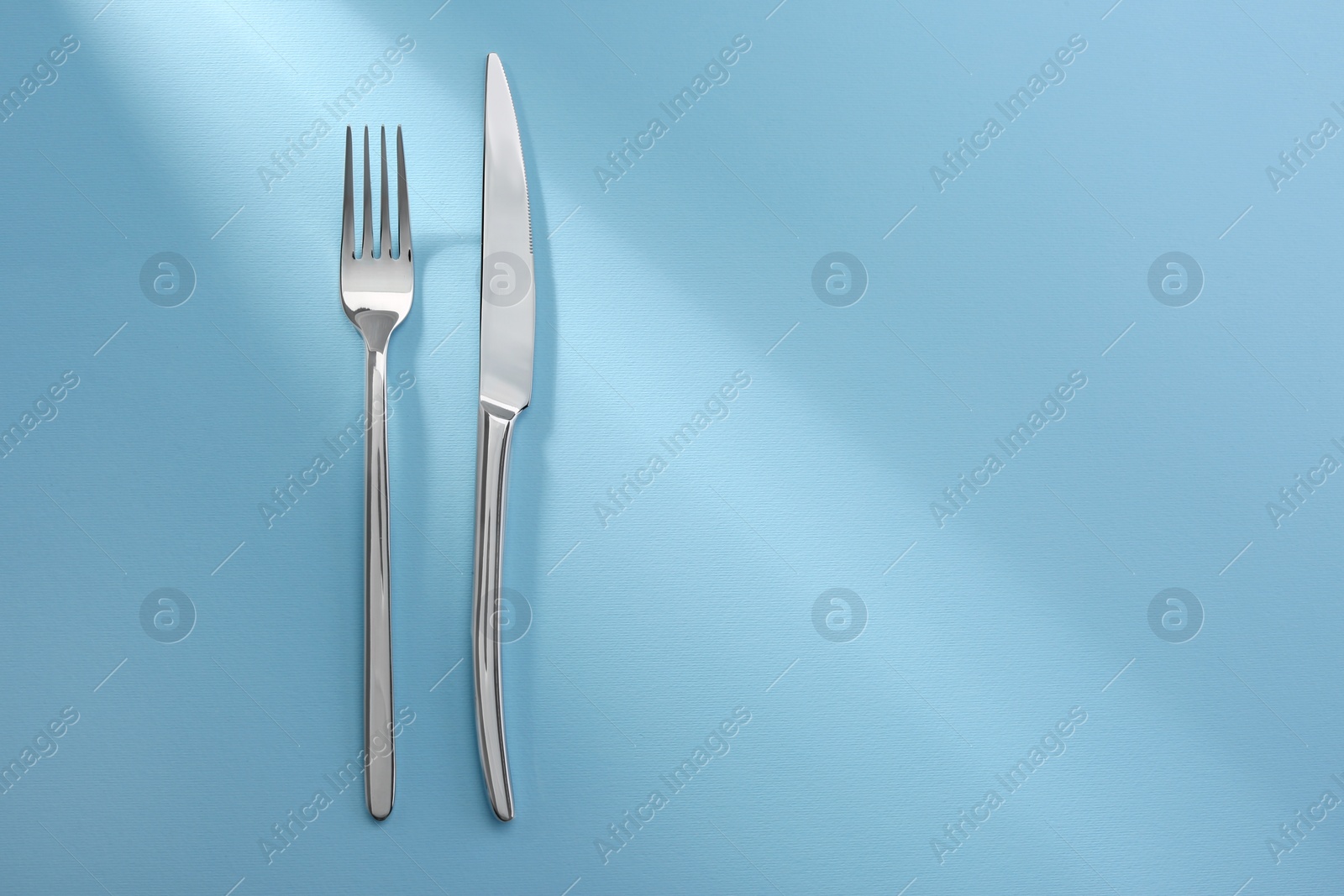 Photo of Shiny fork and knife on light blue background, flat lay. Space for text