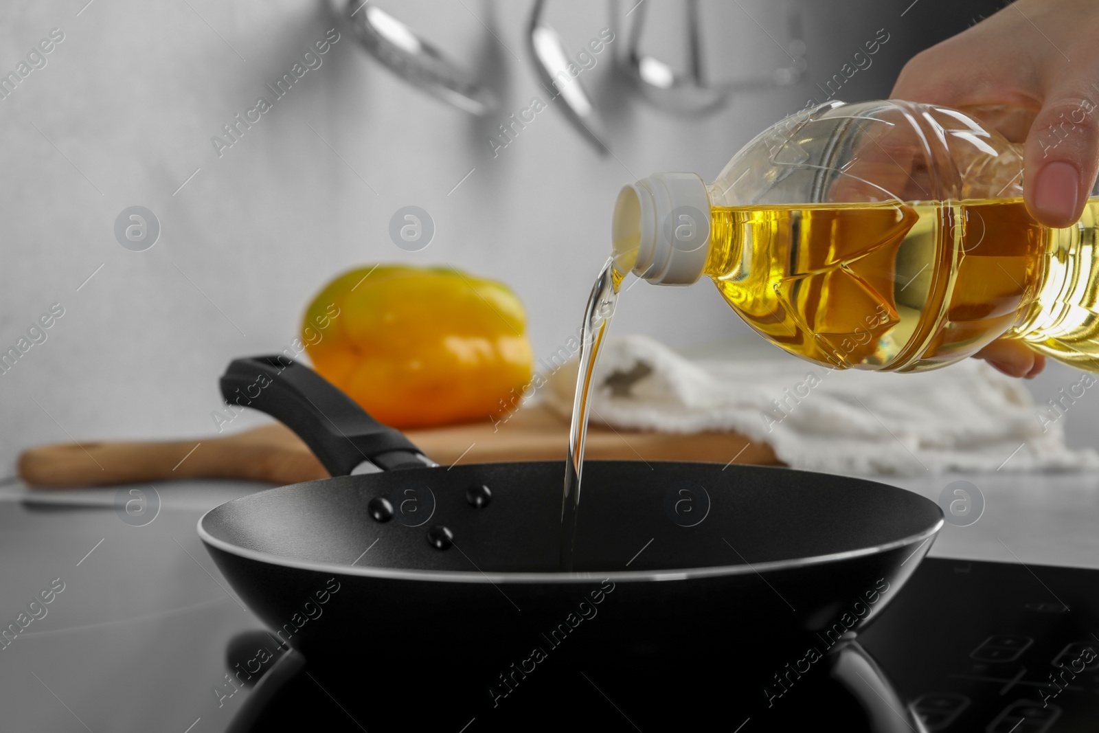 Photo of Woman pouring cooking oil from bottle into frying pan on stove, closeup