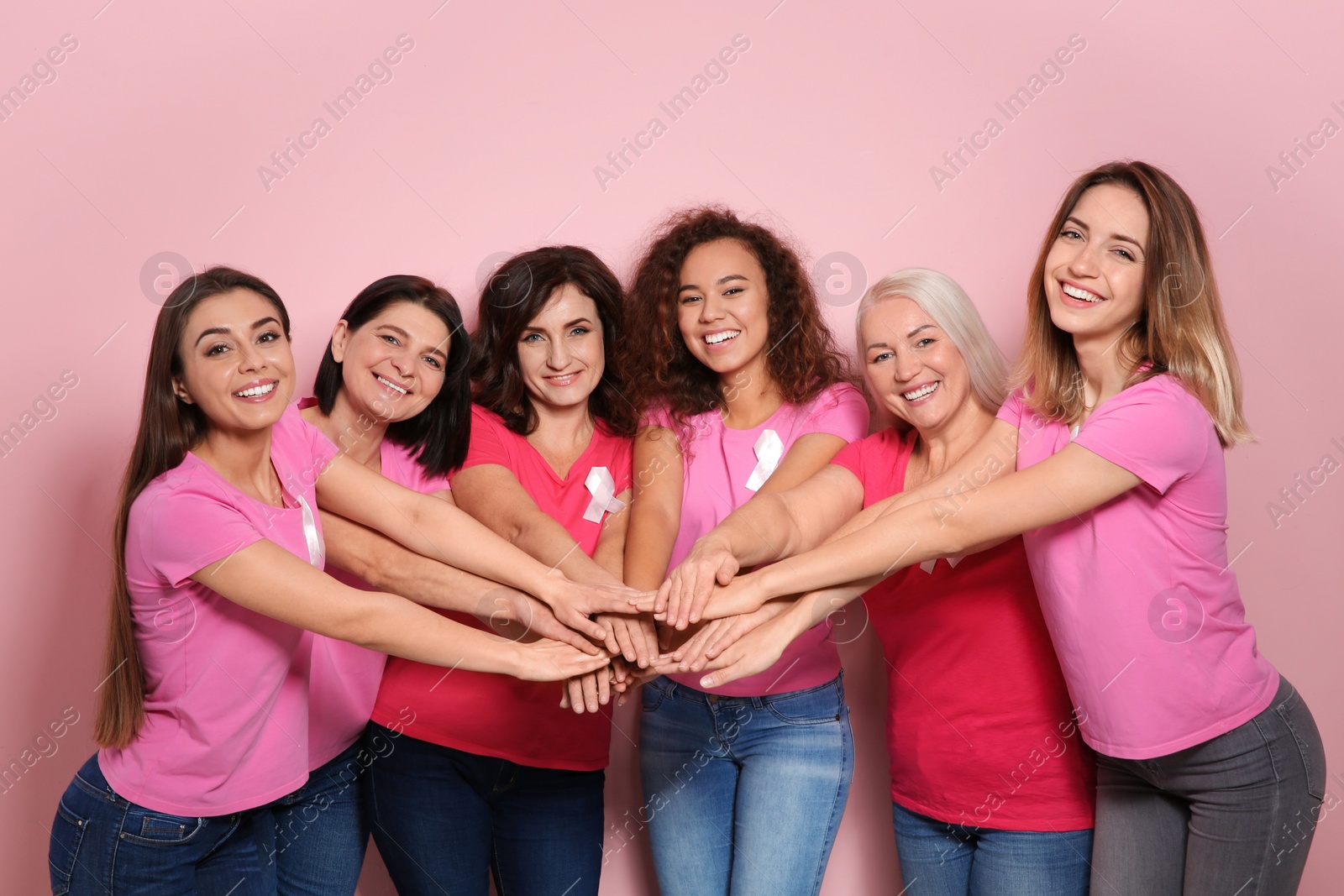 Photo of Group of women with silk ribbons joining hands on color background. Breast cancer awareness concept