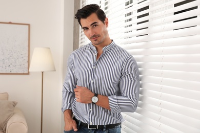 Portrait of handsome young man near window blinds indoors