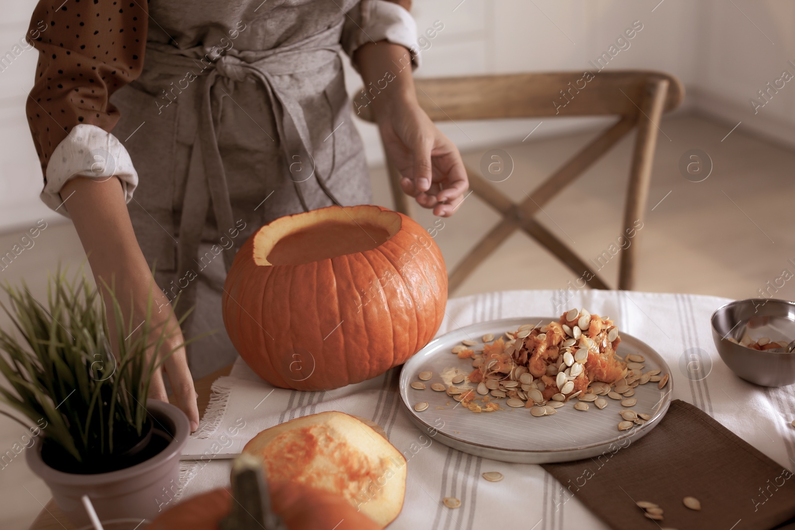 Photo of Woman making pumpkin jack o'lantern at table indoors. Halloween celebration