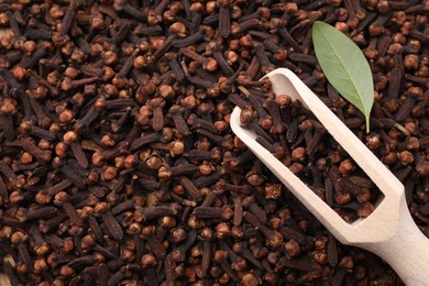 Many aromatic cloves, wooden scoop and green leaf as background, top view