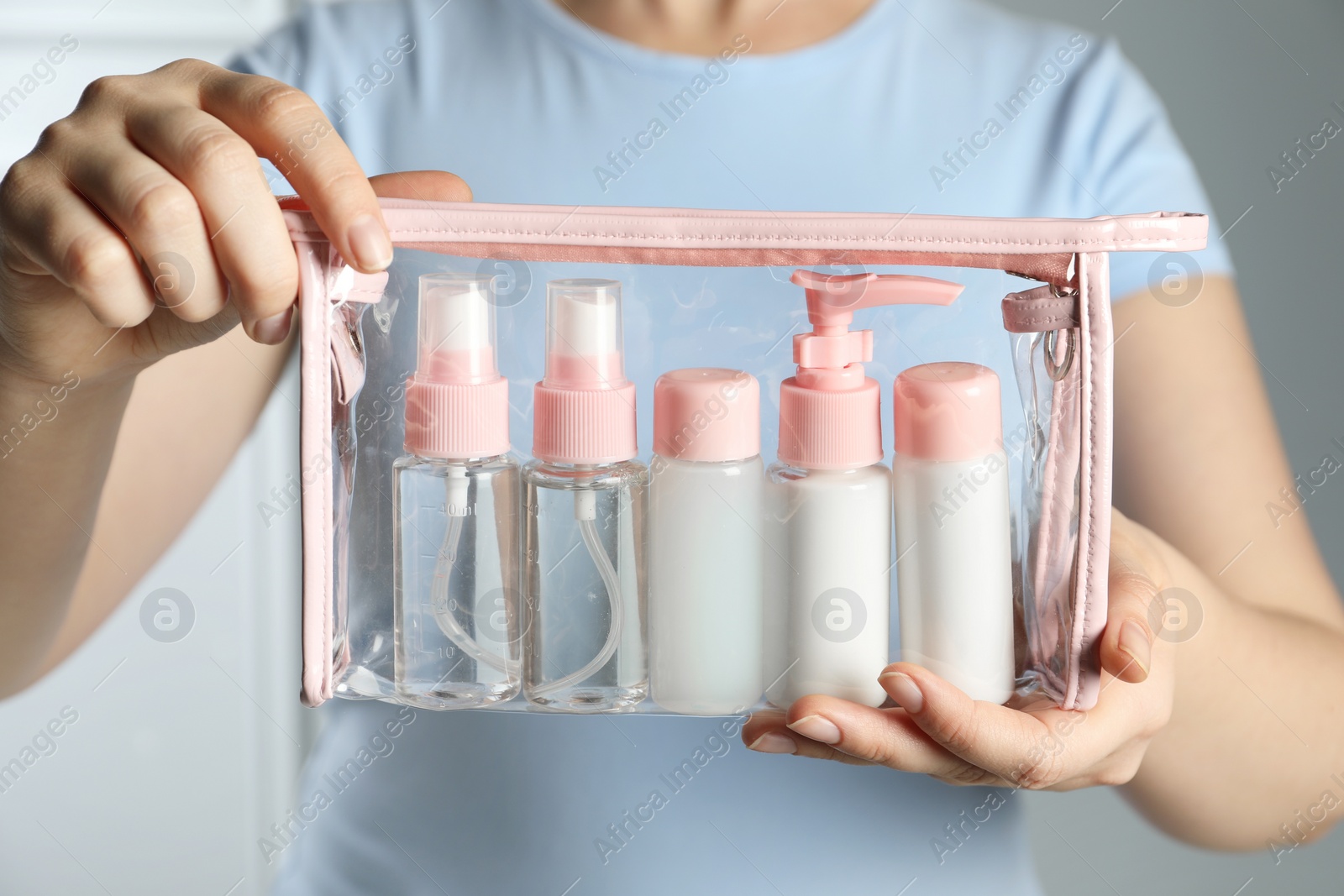 Photo of Woman with cosmetic travel kit on light background, closeup