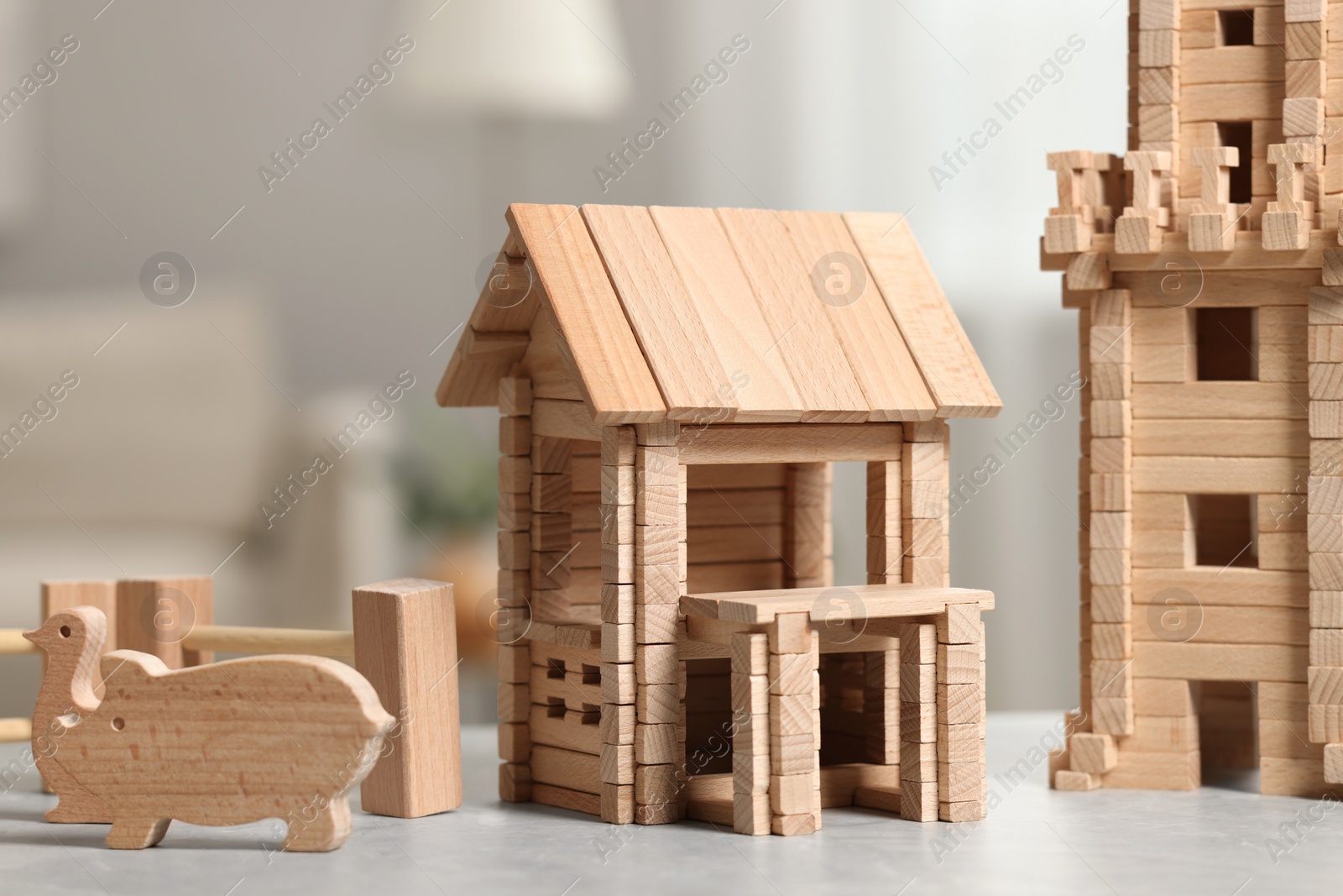 Photo of Wooden house, tower and animals on light grey table indoors, closeup. Children's toys