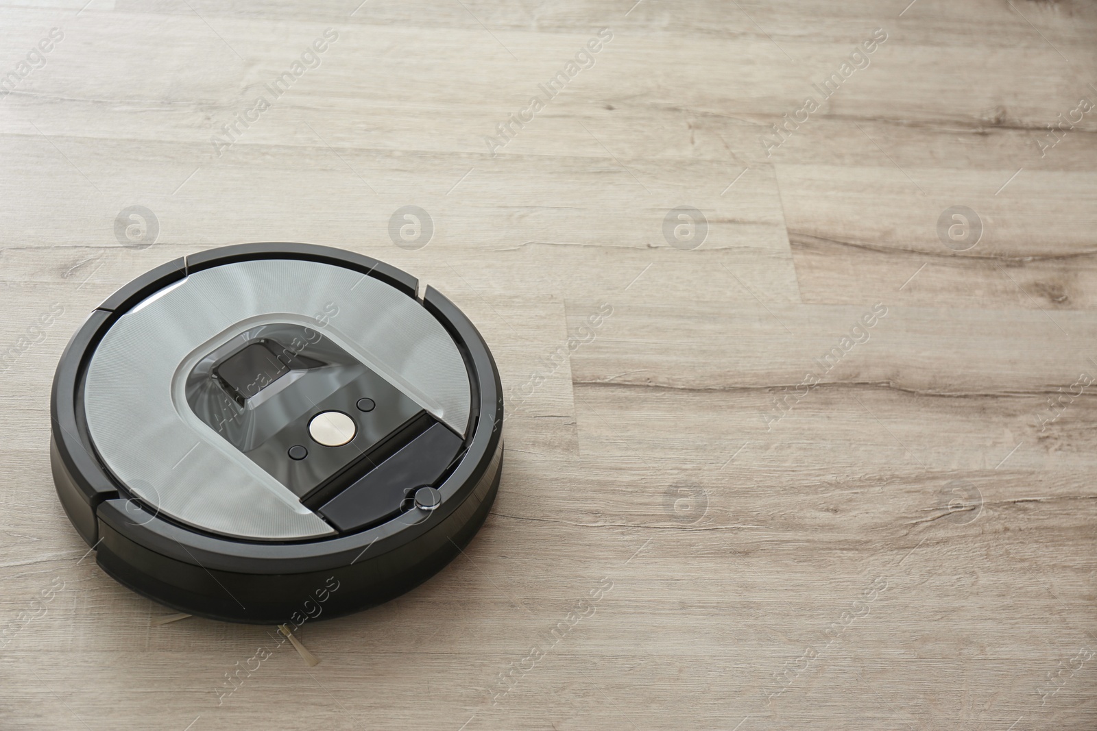 Photo of Modern robotic vacuum cleaner on wooden floor. Space for text