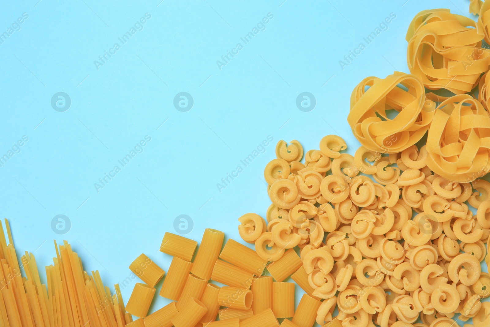 Photo of Different types of pasta on light blue background, flat lay. Space for text